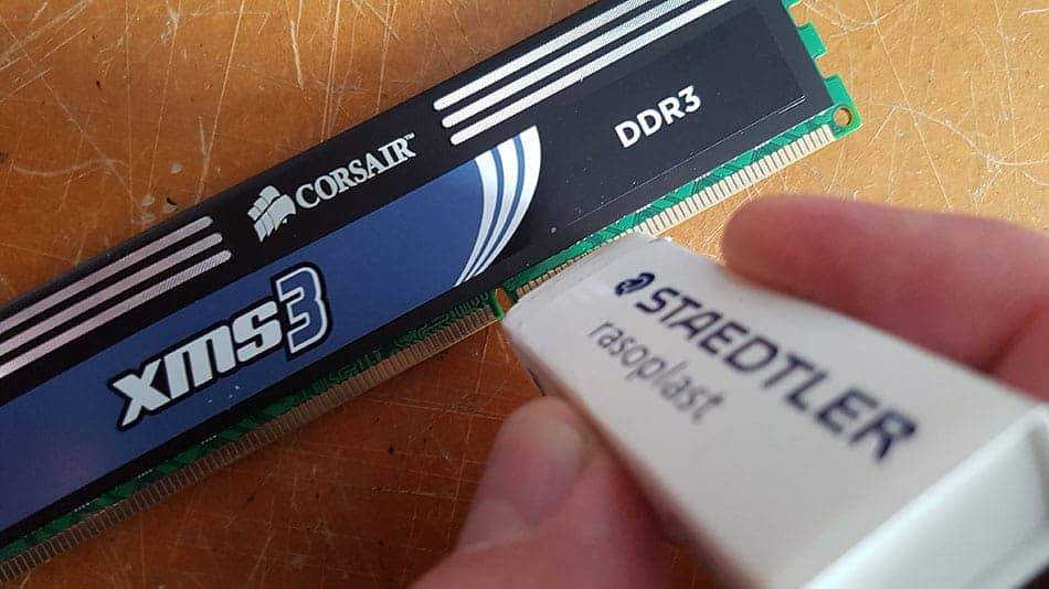 A hand rubbing a white eraser along the gold contact pins of a Corsair DDR3 memory module.